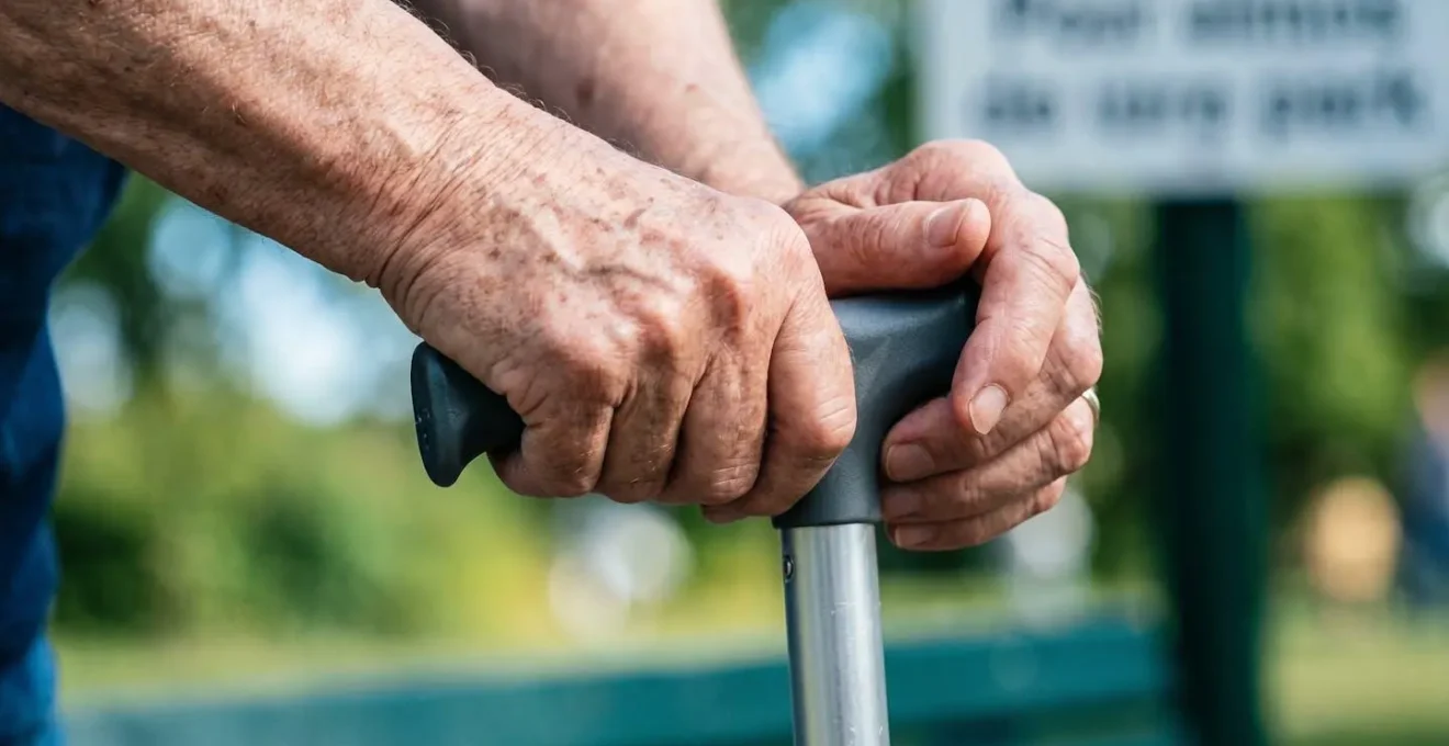 Gros plan sur des mains ridées tenant fermement une canne en appui sur une surface propre et moderne